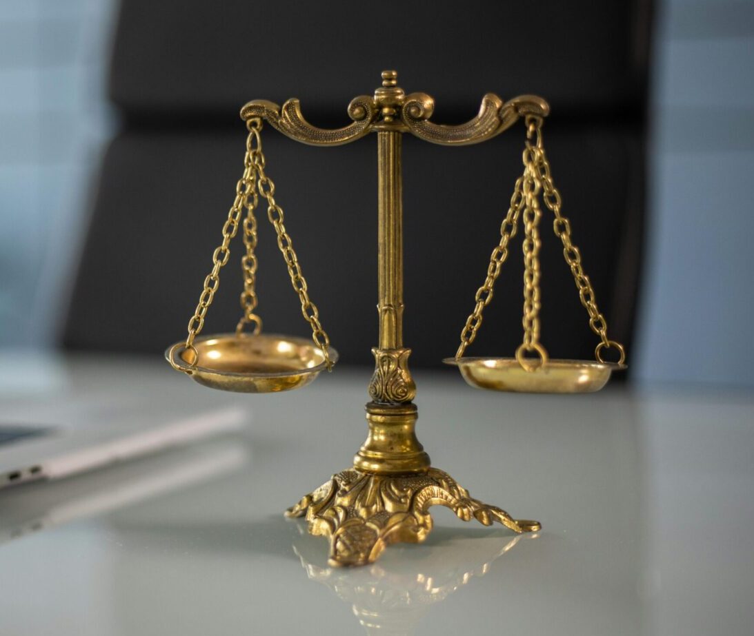 Golden justice scales on a desk beside a laptop, symbolizing law and balance.